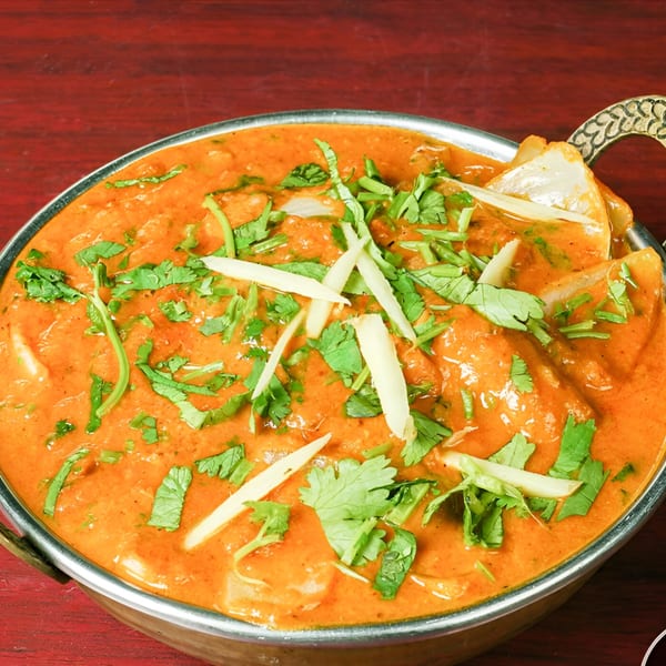 Indian butter chicken curry, garnished with cilantro and ginger, in a metal bowl.