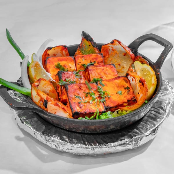 Indian paneer tikka, onions, and lemon wedges in a black cast iron pan.