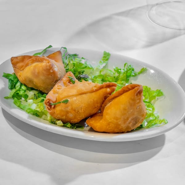 Three golden-brown Indian samosas, garnished with fresh green lettuce, served on a white oval plate.