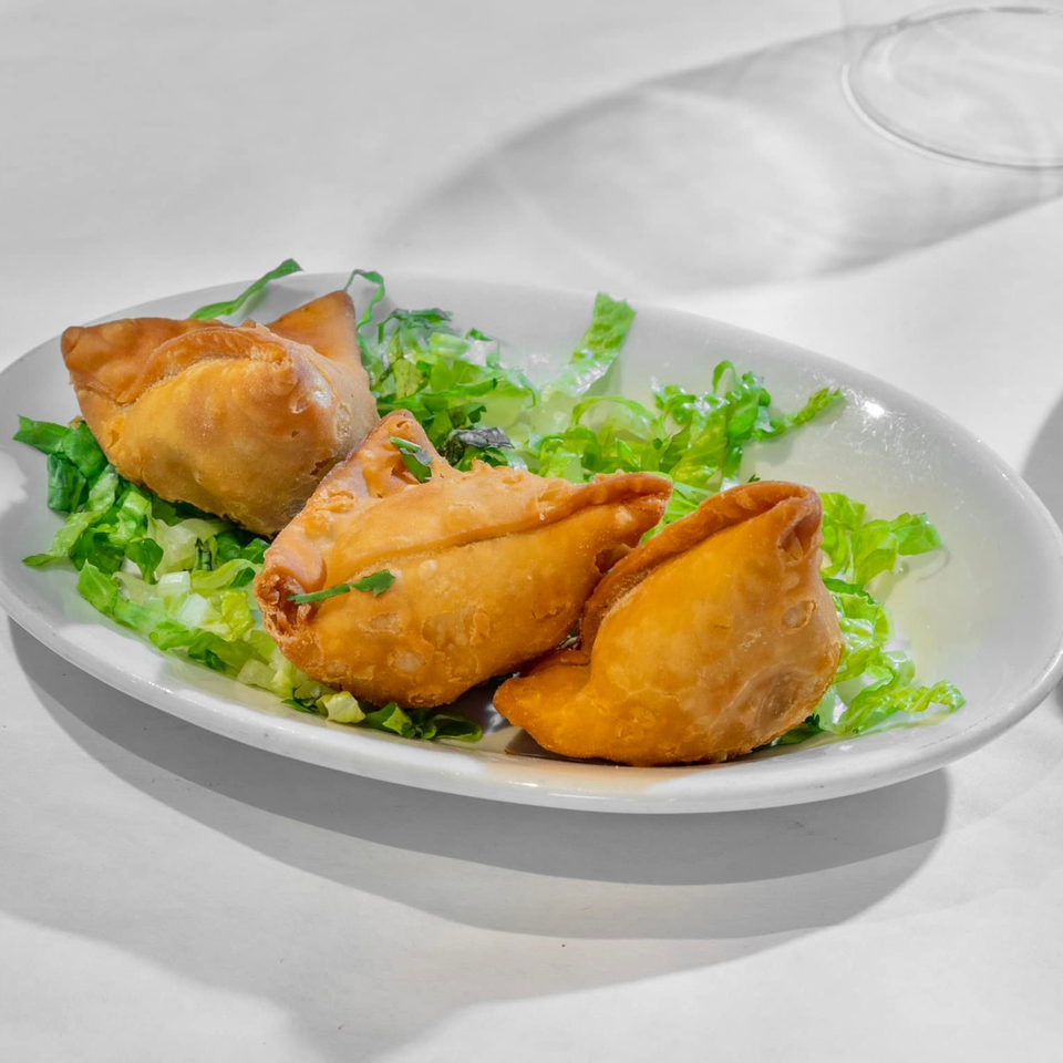 Three golden-brown Indian samosas, garnished with fresh green lettuce, served on a white oval plate.