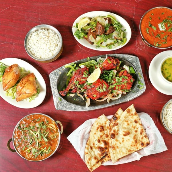 A vibrant spread of Indian dishes, including tandoori chicken, curries, rice, samosas, and naan bread.