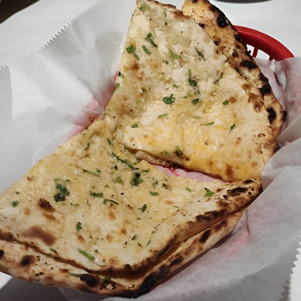 Two pieces of garlic naan bread, garnished with green herbs, in a red basket lined with white paper.