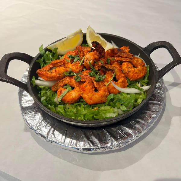 Indian-style shrimp in a black skillet with lettuce, onions, cilantro, and lemon wedges.