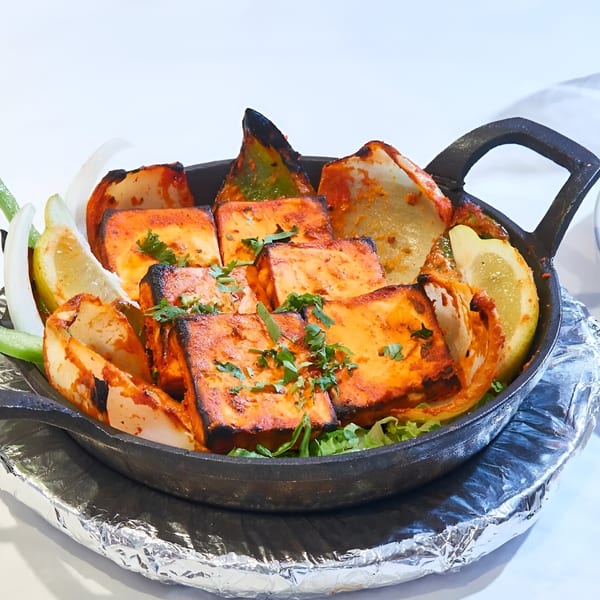 Indian paneer tikka, charred and spiced, served in a black skillet with onions and lemon.