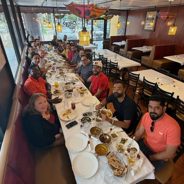 Diverse group of people enjoying Indian food at a long table in Divine Indian Cuisine restaurant.