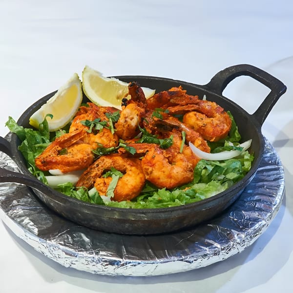 Indian tandoori shrimp with lemon wedges, lettuce, and onions in a cast iron pan.